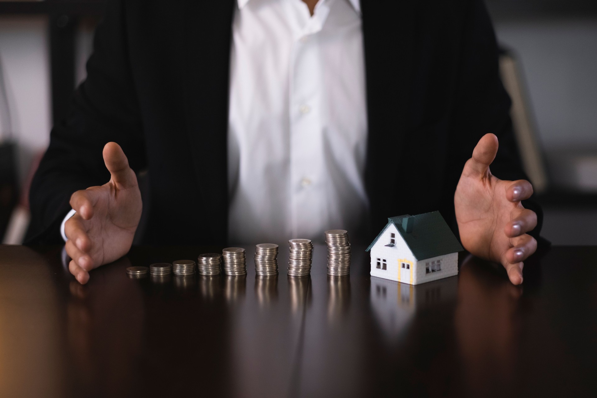 Businesswoman protecting increasing stacks of coins and a miniature house